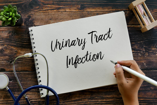 Top view of stethoscope,plant,sand clock, and hand holding pen writing Urinary Tract Infection on notebook on wooden background.