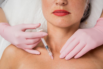 The doctor cosmetologist makes the neckline injections procedure. Young woman in a beauty salon.