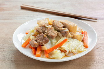 close up of stir fried pork belly with vegetables in a ceramic dish on wooden table. asian homemade style food concept.