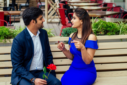 long haired brunette indian woman in blue dress with her handsome boyfriend having dating getting bored .man giving rose to his girlfriend bad relationship in summer downtown street