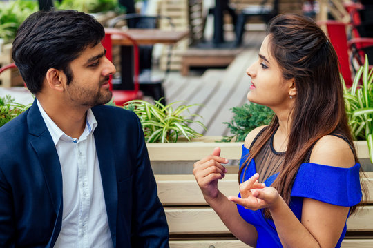 long haired brunette indian woman in blue dress with her handsome boyfriend having dating getting bored .man giving rose to his girlfriend bad relationship in summer downtown street