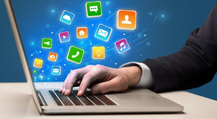 Businessman hand typing on laptop with flying application icons around