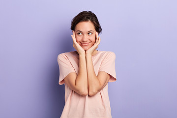 smling cunning sly lovely girl touching cheeks with palms looking aside isolated over blue...