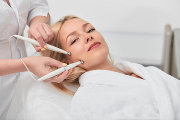 relaxed lovely fair-haired woman in white bathrobe lying and enjoying medical treatment at clinic, close up photo. beauty, face, skin care