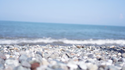 Pebble stones on the shore close up in the blurry light in the distance background.