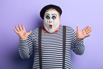portrait of an amazed clown with painted white face, open mouth, bugged eyes and raised arms performing on the stage. close up portrait, facial expression