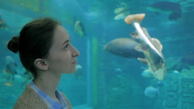 Underwater life, tourism, education and entertainment concept. Portrait of woman looking at fish vortex in large public aquarium tank at Oceanarium