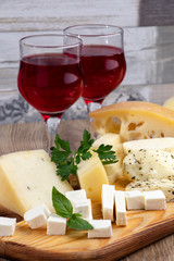Different types of cheeses with a glass of wine on a wooden cutting board