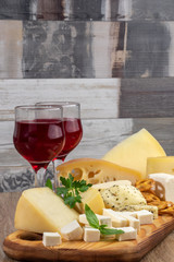 Different types of cheeses with a glass of wine on a wooden cutting board. Copy space
