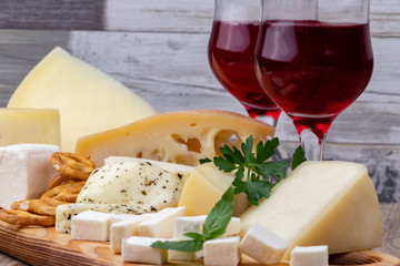 Different types of cheeses with a glass of wine on a wooden cutting board