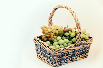 Green and blue grapes in a wicker basket on white background, autumn harvest.