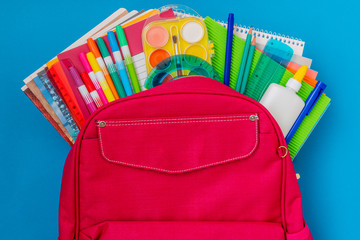 Backpack with school supplies on the blue background