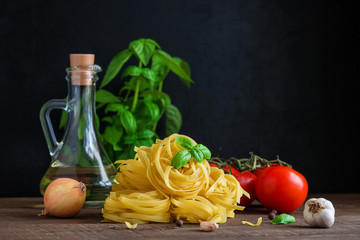 raw ingredients for cooking italian pasta. fettuccine tomatoes garlic basil olive oil onion on wooden table copy space