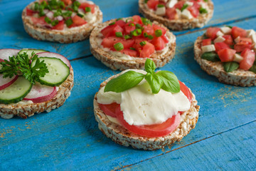 homemade  rice  cakes with mozzarella tomatoes basil and chopped vegetables on blue wooden table close up