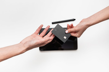 Close up top view of a woman hands over bank card to a man in order to pay for the product. Tablet and pen on a white table. Concept of online shopping. Successful deal.