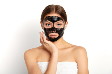 pleasant young woman applying a mask on her face, close up portrait, isolated white background, studio shot,