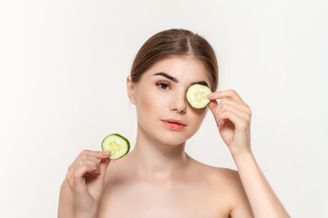Close-up portrait of a beautiful young girl holding slices of  green cucumber close to eyes isolated over white background.