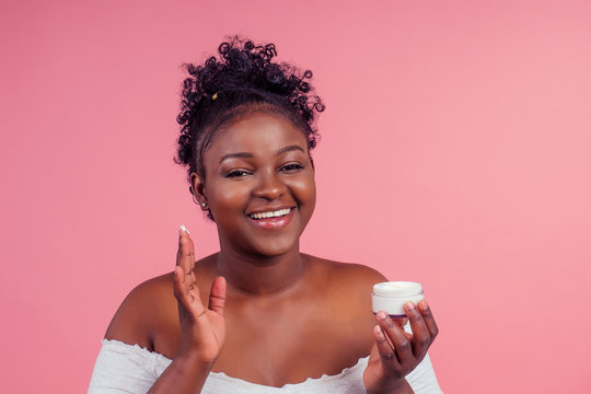 Beautiful Woman Flawless Skin Smooth Complexion Applying Moisturiser Face Cream To Her Cheek, Beauty Cosmetics Skincare Concept In Studio Pink Background