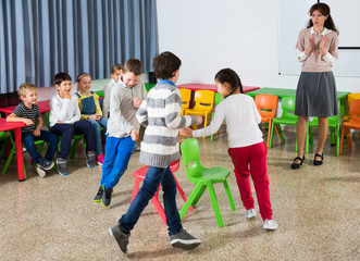 Obraz premium Kids and teacher playing musical chairs