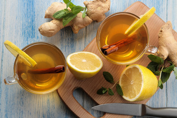 Tea with lemon and a cinnamon stick with ginger and mint in glass cups on a brown wooden table. a warming drink. Autumn or winter drink. top view