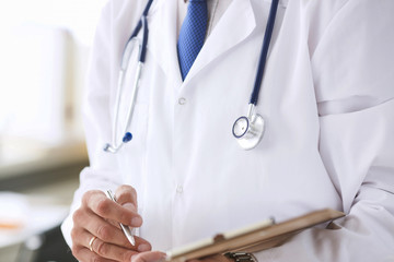 Close-up of clipboard with blank paper in medical doctor hand. Male doctor listens to the patient holding a clipboard with documents for hospitalization.