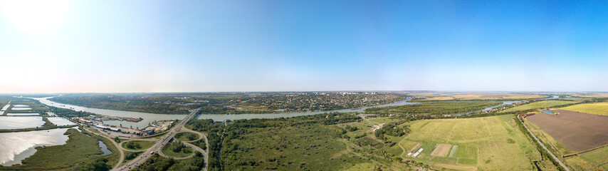 Fototapeta na wymiar Aerial view (drone view) on a sunny summer day over the Don River at the intersection with the M4-Don motorway. Road junction, bridge and port. The high right bank and the city of Aksai on its hills