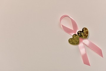 A pink satin ribbon fastened with a clothespin with two golden hearts on a light background in the lower right corner.