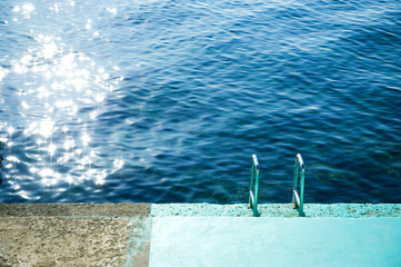 descent into the sea from a concrete slab with a chrome staircase partially painted blue
