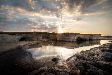 Shot of the sun rising behind the rocks at Cirica Bay at sunrise. Cirica is a beautiful nature seaside place made of cliffs, rocks and sand in the southern Sicily, Italy	
