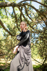 Young beautiful elegant girl in black vintage dress with veil posing among trees outdoor.