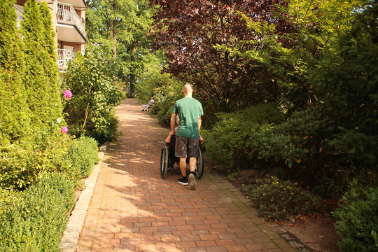 Young Man Carries An Elderly Overweight Woman In A Wheelchair On The Street