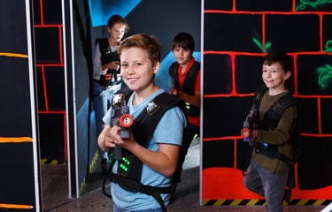 Emotional teen boy with laser pistol playing laser tag with friends on dark labyrinth