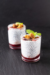 Healthy food concept Chia seeds, milk pudding with goji, white mulberry and mix dried seeds in small Glass on black slate board background