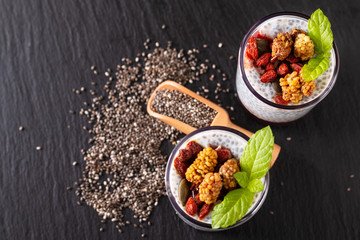 Healthy food concept Chia seeds, milk pudding with goji, white mulberry and mix dried seeds in small Glass on black slate board background