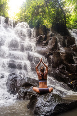 Woman practices yoga near waterfall in Bali, Indonesia