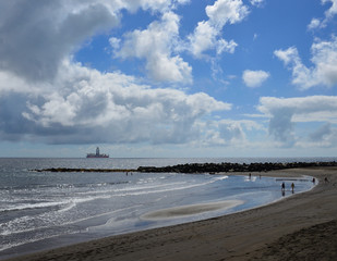 Fototapeta na wymiar Sandy beach with people walking on the shore, blue sky with clouds and ship, La laja, coast of Las Palmas de Gran Canaria 