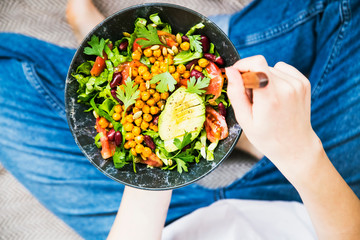 Clean eating, vegan healthy salad bowl , top view of woman holding salad bowl, plant based healthy diet with greens,avocado, salad, chickpeas and vegetables