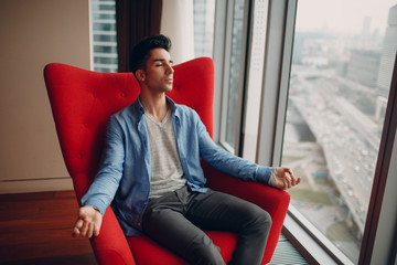 Portrait of stylish young man sitting in chair and meditate