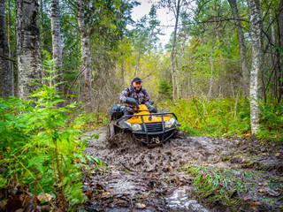 Quad biking. ATV mud. Man rides a quad bike front view. Man in a yellow helmet on an quadrocycle. Riding an ATV after rain. Traveling through the woods on an quadrocycle. Riding through the mud.