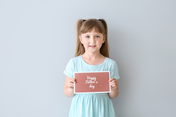 Fototapeta na wymiar Cute little girl with greeting card for Father's Day on light background