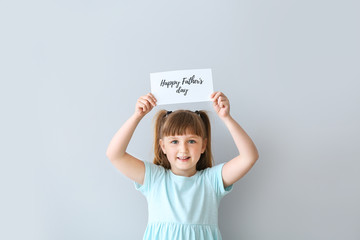 Cute little girl with greeting card for Father's Day on light background