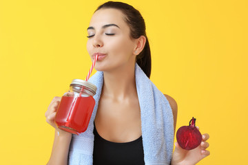 Young sporty woman drinking healthy beet juice on color background