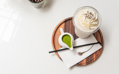 Frappe coffee with whipped cream on top serving with matcha green tea cream ready to pour on top of coffee. Picture with copy space on white table.