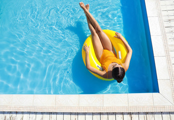 Beautiful young woman relaxing on inflatable ring in swimming pool