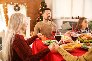 Family praying before having Christmas dinner at home