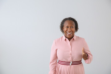 Portrait of African-American woman showing thumb-up on light background