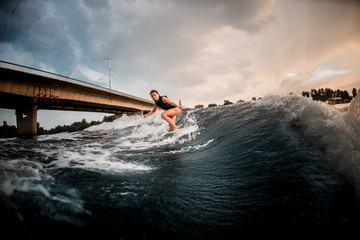 Sporty girl riding on the wakeboard on the river in the background of the bridge