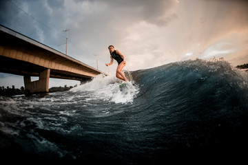 Slim fit girl riding on the wakeboard on the river in the background of the bridge