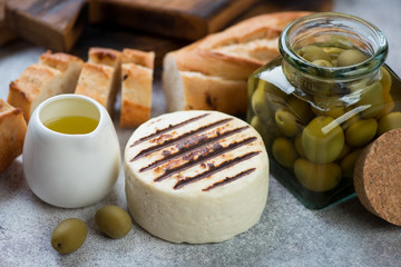 Whole grilled cheese with baguette and green olives, close-up, selective focus
