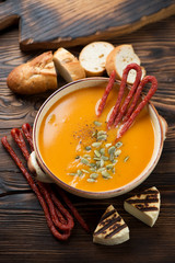 Bowl of pumpkin cream-soup with smoked meat, baguette and grilled cheese in a rustic wooden setting